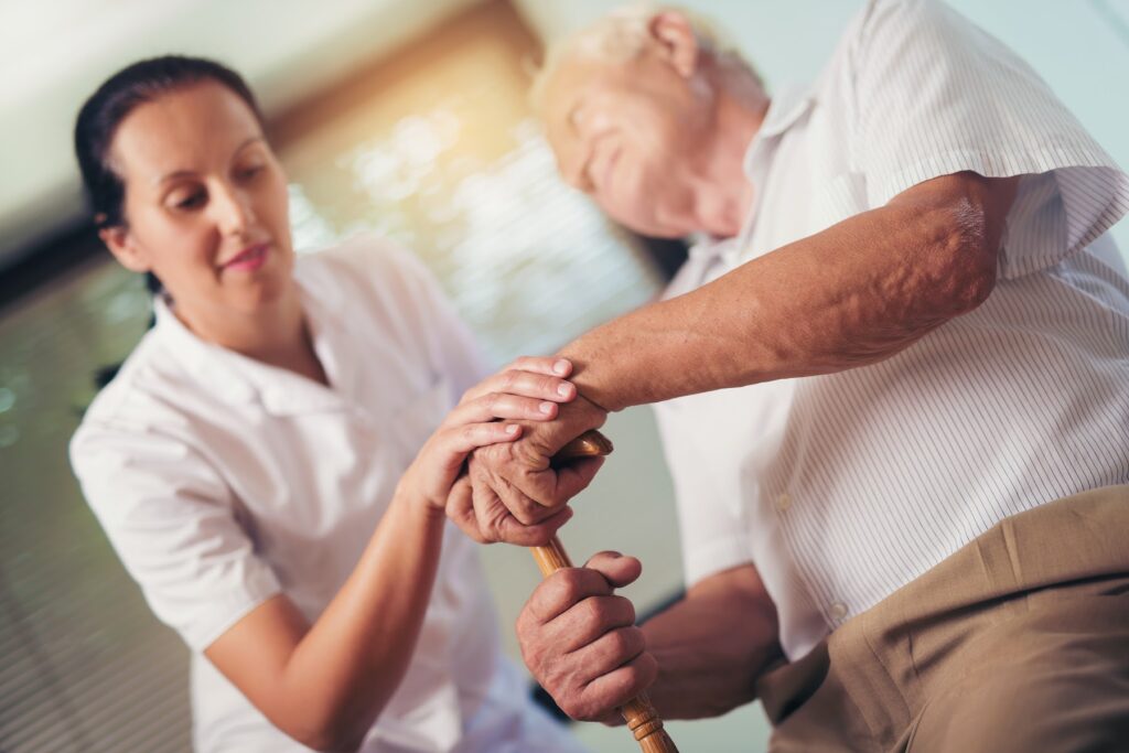 Therapist resting her hand on an older man's hand as he holds a walking stick
